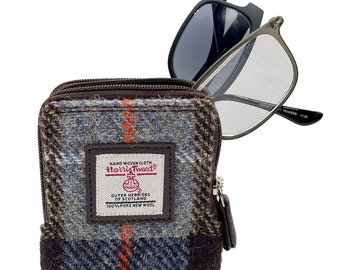 May include: A brown tweed glasses case with a zipper closure. The case has a label that reads "HAND WOVEN CLOTH Harris Tweed OUTER HEBRIDES OF SCOTLAND 100% PURE NEW WOOL". A pair of glasses is partially sticking out of the case.