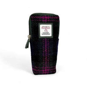 Peut inclure: Une trousse rectangulaire à fermeture éclair en tissu de laine sombre avec un motif à carreaux noir, bleu marine et magenta. Une étiquette blanche rectangulaire sur le devant porte le texte Harris Tweed, Hand Woven Cloth, Outer Hebrides of Scotland, 100% Pure New Wool.