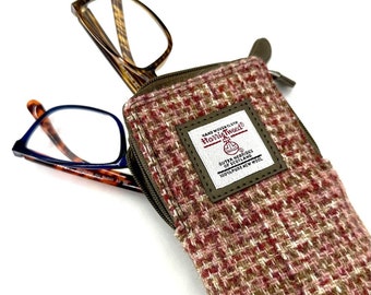 May include: A brown and pink tweed glasses case with a zipper closure. The case has a leather patch with the text "Harris Tweed" and "Outer Hebrides of Scotland 100% Pure New Wool".