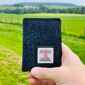 May include: A black leather wallet with a blue and black tweed pattern. The wallet has a label that reads "HAND WOVEN CLOTH Harris Tweed® OUTER HEBRIDES OF SCOTLAND 100% PURE NEW WOOL".