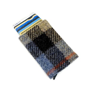May include: A rectangular, plaid card holder in shades of blue, tan, and black. A patterned card is partially visible inside the holder. The card holder has a black zipper closure.