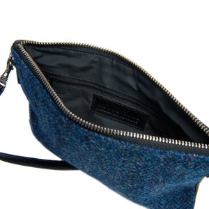 Op de afbeelding: Een blauwe tweed clutch met een zwarte leren band en een zilveren rits. De tas is gevoerd met zwart en heeft een klein binnenvak.