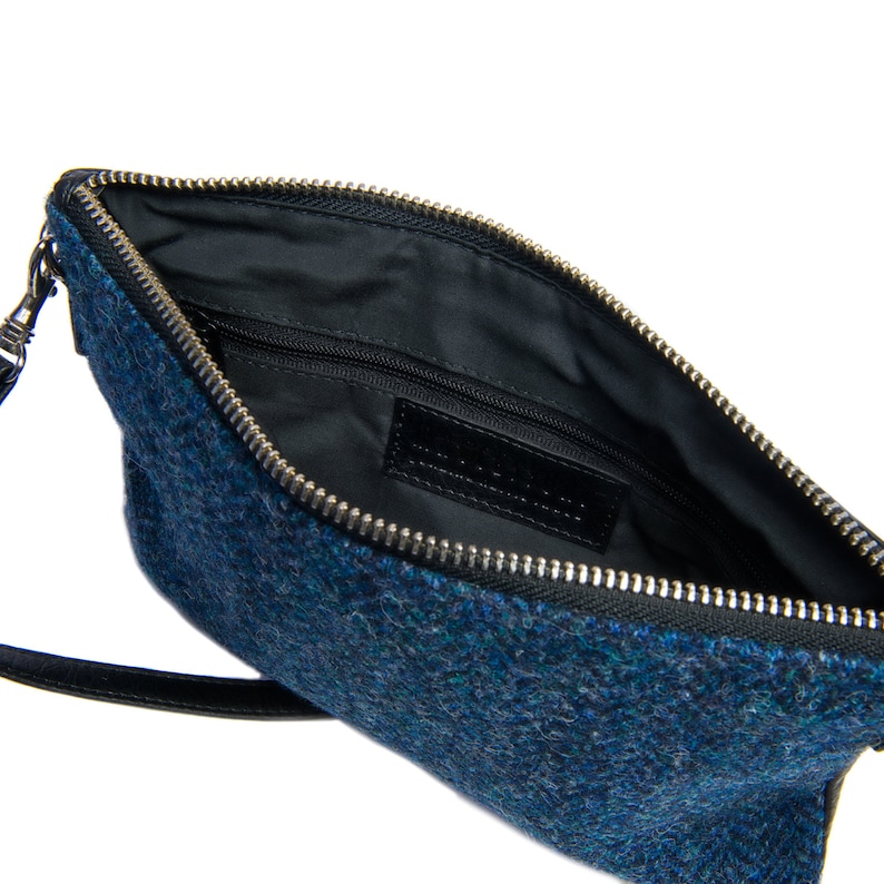 Op de afbeelding: Een blauwe tweed clutch met een zwarte leren band en een zilveren rits. De tas is gevoerd met zwart en heeft een klein binnenvak.