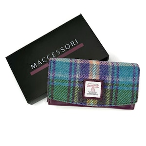 May include: A plaid wallet with teal, purple, and green hues, resting next to a black box with the word "MACCCESSORI" in white. The wallet has a leather base and a "Harris Tweed" label.