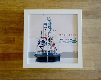 May include: A white framed print with a colorful illustration of a carousel ride. The text "Pepsi-Cola presents Walt Disney's 'it's a small world' UNICEF" is at the bottom of the print.