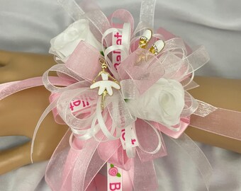 May include: A wrist corsage featuring white roses, pink and white ribbons, and a gold ballerina charm. The ribbons are printed with the word "Ballet". Two small gold ballet shoe charms are also included.