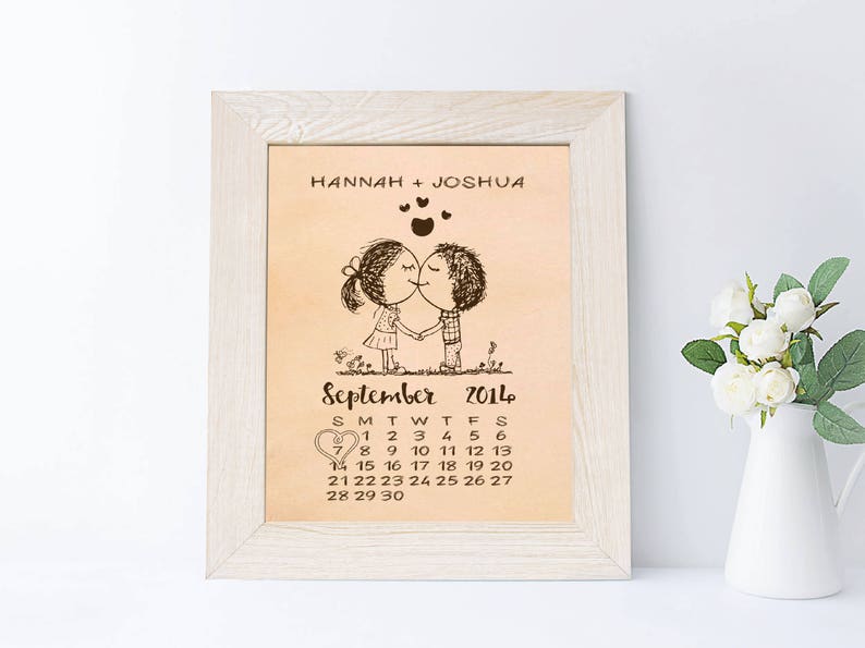 May include: A framed print with a light brown background featuring a cartoon couple kissing with hearts above them. The print includes the text "HANNAH + JOSHUA" and a calendar for September 2014.