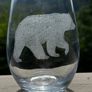 May include: A clear glass wine glass with an etched design of a black bear walking. The bear is facing the right side of the glass.