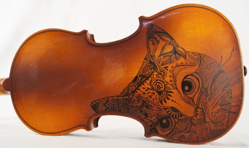 May include: A wooden violin with a black and white intricate design of a cat's face on the body.