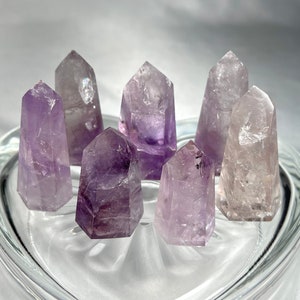 May include: Six amethyst crystal points in various shades of purple and clear, arranged in a circle on a clear glass surface.