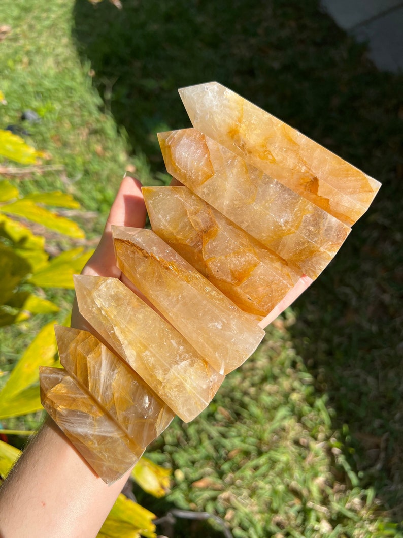 May include: A set of seven golden citrine crystal points, stacked in a graduated size, with a clear, translucent appearance and a slight golden hue.
