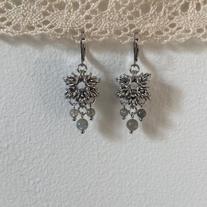 Może przedstawiać: Srebrne kolczyki z geometrycznym wzorem i zwisającymi szarymi kamieniami.
