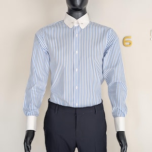 May include: A mannequin wearing a black hat, a blue and white striped shirt with a white collar and cuffs, and black pants. The shirt has vertical stripes. The mannequin is wearing black gloves.