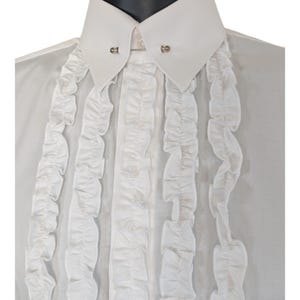 Op de afbeelding: Een wit formeel overhemd met een klassieke kraag en decoratieve ruches aan de voorkant. Het overhemd heeft een speld op de kraag. De ruches geven het kledingstuk een vleugje elegantie.