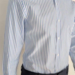 May include: A blue and white striped dress shirt with a white collar and cuffs. The shirt is buttoned up and paired with black dress pants. The shirt is on a mannequin.