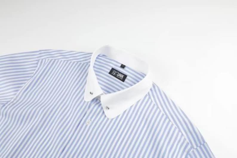 May include: A blue and white striped dress shirt with a white collar. The shirt has a classic design with a button-down front and a small label that reads "77 UNIK". The shirt is made of a lightweight fabric.