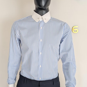 May include: A black hat sits atop a mannequin wearing a blue and white striped shirt with a white collar and cuffs. The mannequin is also wearing dark blue pants. A gold clock is visible in the background.