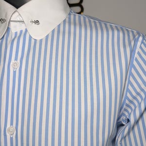 May include: A blue and white striped dress shirt with a white collar and buttoned cuffs. The shirt has a classic design with vertical stripes and a collar pin.