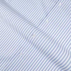 May include: Close-up of a light blue and white striped fabric. The fabric is a woven material with vertical stripes. The image shows the fabric's texture and the subtle variations in the stripes. Several white buttons are visible.