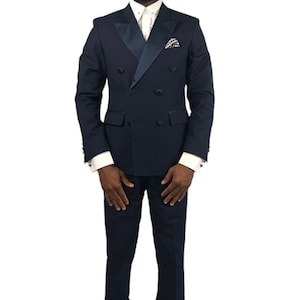Op de afbeelding: Een marineblauw dubbelbreasted pak met een satijnen revers, gecombineerd met een wit overhemd en een zwarte hoed. Het pak heeft een pochet en wordt gedragen met zwarte schoenen. Een formele outfit.
