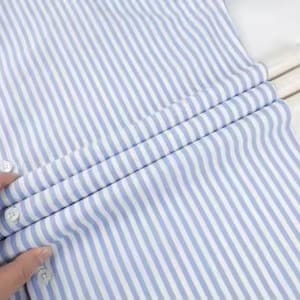 May include: A blue and white striped button-down shirt. The shirt is made of a lightweight fabric and features vertical stripes. The buttons are white. The shirt is folded over a white hanger.
