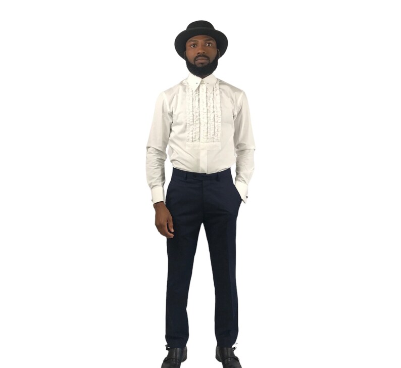 Op de afbeelding: Een formele outfit met een wit overhemd met een gerimpelde voorkant, gecombineerd met marineblauwe broek. De outfit wordt gecompleteerd met een zwarte hoed. Het overhemd heeft lange mouwen en de broek heeft een klassieke pasvorm.