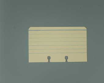 May include: Cream-colored index card with blue horizontal lines and a blue top line. The card has two cut-out notches at the bottom and rounded corners. The card is on a gray background.