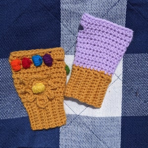 May include: Two crocheted fingerless gloves, one in a light purple color and the other in a brown color. The brown glove has a design that resembles the Infinity Gauntlet from the Marvel Cinematic Universe. The glove has six colorful gems.