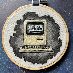 May include: Embroidered artwork of a vintage beige computer with a black and white keyboard. The screen displays the word "Hello" in a blue font.