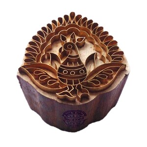 Puede incluir: Un sello de impresión de bloque de madera con un diseño de latón de un pavo real en un patrón floral. El sello está etiquetado como "Made in India" y "Royal Kraft".