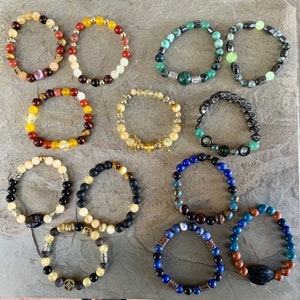 Pode incluir: Uma coleção de 10 pulseiras de contas coloridas com vários detalhes de pedras preciosas e metal. As pulseiras apresentam uma variedade de cores, incluindo azul, verde, vermelho, amarelo e preto.