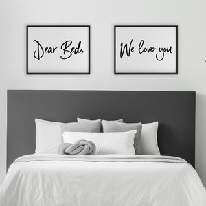 Puede incluir: Dos cuadros enmarcados con marcos negros y fondos blancos. El marco izquierdo dice "Dear Bed," y el marco derecho dice "We love you" en escritura negra. Debajo, una cama con ropa de cama blanca y almohadas grises.