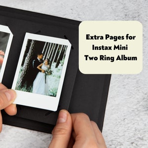 May include: A black photo album with two Instax Mini wedding photos. The album features a two-ring binder. Text on a cream label reads "Extra Pages for Instax Mini Two Ring Album".