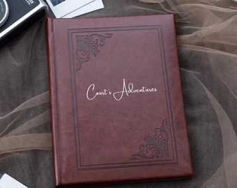 Könnte beinhalten: Ein braunes Lederfotoalbum mit einem dekorativen Design und dem Text "Court's Adventures" in weiß auf der Vorderseite geprägt.