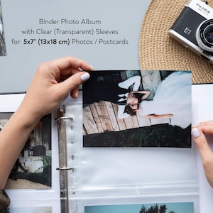 May include: A black binder photo album with clear sleeves holding a 13x18 cm photo. The photo shows a couple lying down. A vintage camera sits on a woven mat. The text reads: "Binder Photo Album with Clear (Transparent) Sleeves for 5x7" (13x18 cm) Photos / Postcards."