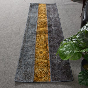 May include: A long, narrow runner rug with a gray background and a yellow and orange patterned stripe down the center.