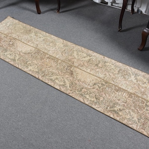 May include: A rectangular beige rug with a floral pattern. The rug has a distressed look with faded colors and a central seam. The rug is placed on a gray surface.