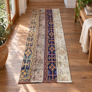 May include: A rectangular runner rug featuring a patchwork design with vertical stripes of varying patterns. The rug displays a mix of blue, yellow, orange, brown, and cream colors with geometric motifs and floral scrollwork, finished with short fringe.