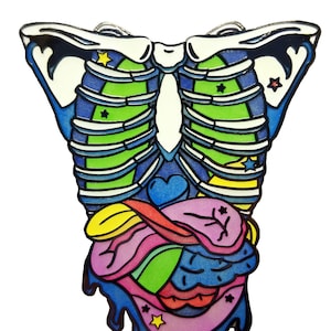May include: A colorful enamel pin depicting a human ribcage with a heart, lungs, and other internal organs. The organs are stylized and dripping with blue, pink, and yellow paint. The pin has a black outline and stars scattered throughout.