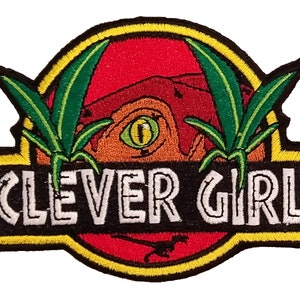 May include: Embroidered iron-on patch with a green, red, and orange dinosaur silhouette with the text "CLEVER GIRL" in white letters on a black background.