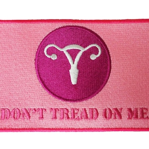 May include: A pink embroidered patch with a uterus graphic inside a magenta circle. The patch reads "DON'T TREAD ON ME" in pink text, with a pink border.