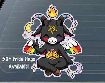 May include: A black cartoon goat with rainbow wings and a pentagram on its forehead, sitting in a meditative pose with a golden symbol in its lap. The goat has a pink heart on each cheek and is surrounded by stars and crescent moons. The text "50+ Pride Flags Available!" is at the bottom of the image.