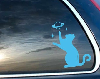 May include: A blue cat silhouette reaching up to a blue planet with a ring around it. There are three small white stars around the planet.