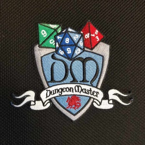 May include: Embroidered patch featuring a shield design with the letters "DM" in blue, a banner reading "Dungeon Master," and dice. The patch includes a green six-sided die, a blue twenty-sided die, and a red four-sided die. A red dragon is also featured.
