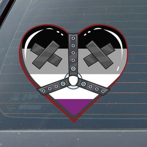 May include: A heart-shaped sticker with a black, gray, and white asexual pride flag design. The heart has a black leather harness with a silver ring and a purple stripe at the bottom.
