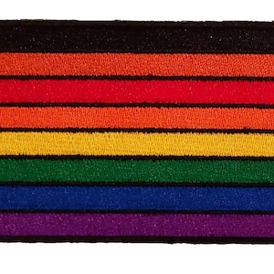 May include: A rainbow pride flag patch with eight horizontal stripes in the colors black, orange, red, orange, yellow, green, blue, and purple. The patch is embroidered and has a black border.