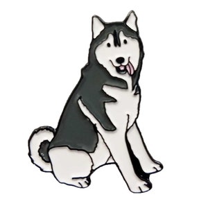 May include: A black and white enamel pin shaped like a sitting Siberian Husky dog. The dog has pointed ears, a curled tail, and a pink tongue sticking out of its mouth. The design features bold black outlines and a smooth, glossy finish.