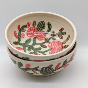 Puede incluir: Dos cuencos de cerámica blanca con un diseño floral verde y rojo. Los cuencos están apilados uno encima del otro.