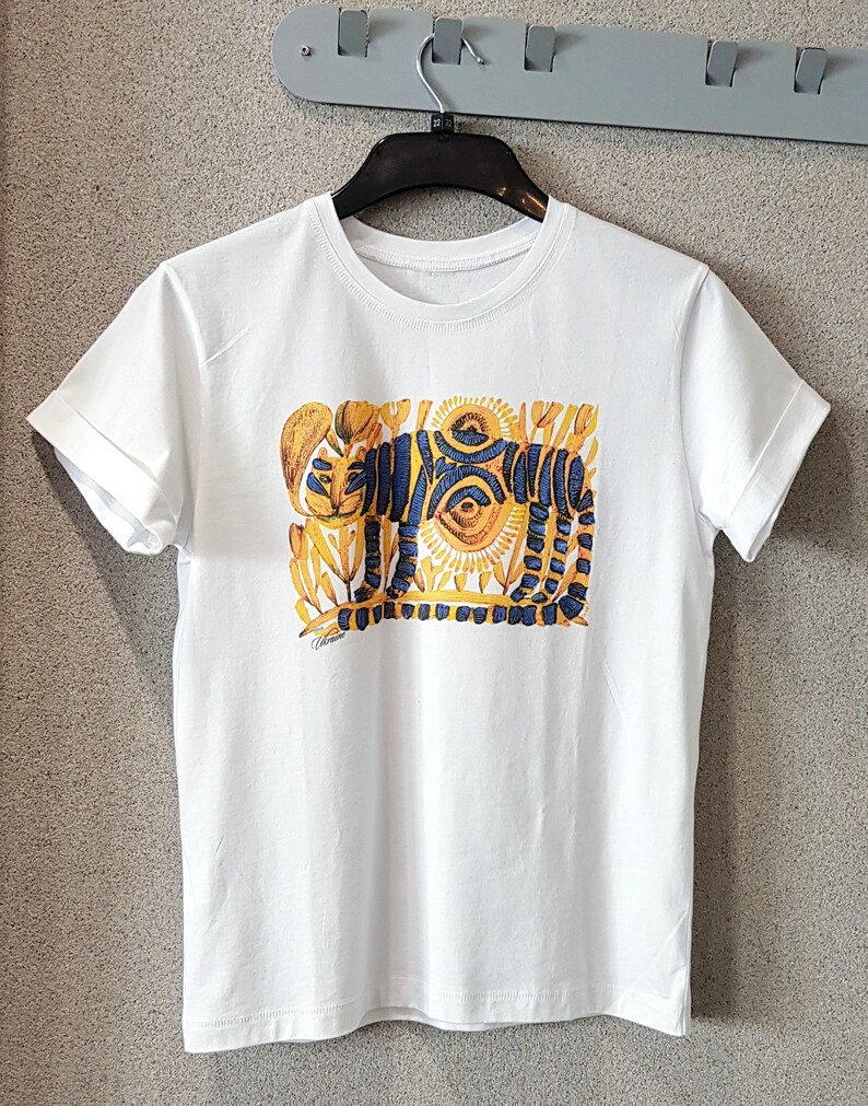 Op de afbeelding: Wit T-shirt met een kleurrijke afbeelding van een tijger met gele, blauwe en oranje details. De tijger is omringd door gestileerde bloemen en bladeren.