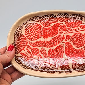 May include: A ceramic oval serving tray with a hand-painted design of stylised flowers and leaves in shades of red and brown.